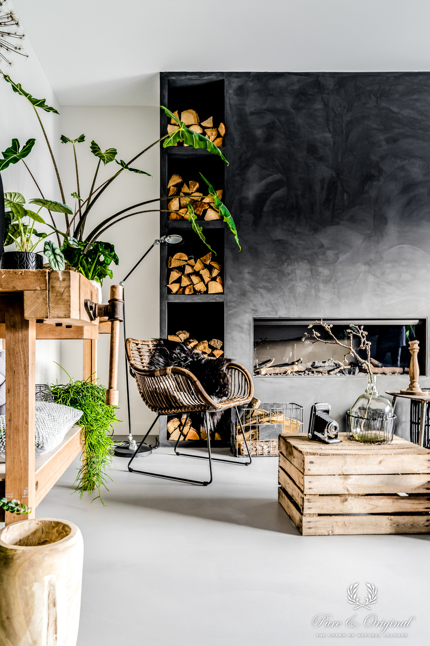 Modernes Wohnzimmer mit dunkler Kaminwand in Slate Grey, Holzregal, Loungesessel und grünen Pflanzen